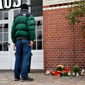 Ein Mann steht vor einem Backsteingebäude vor dem Blumen niedergelegt wurden