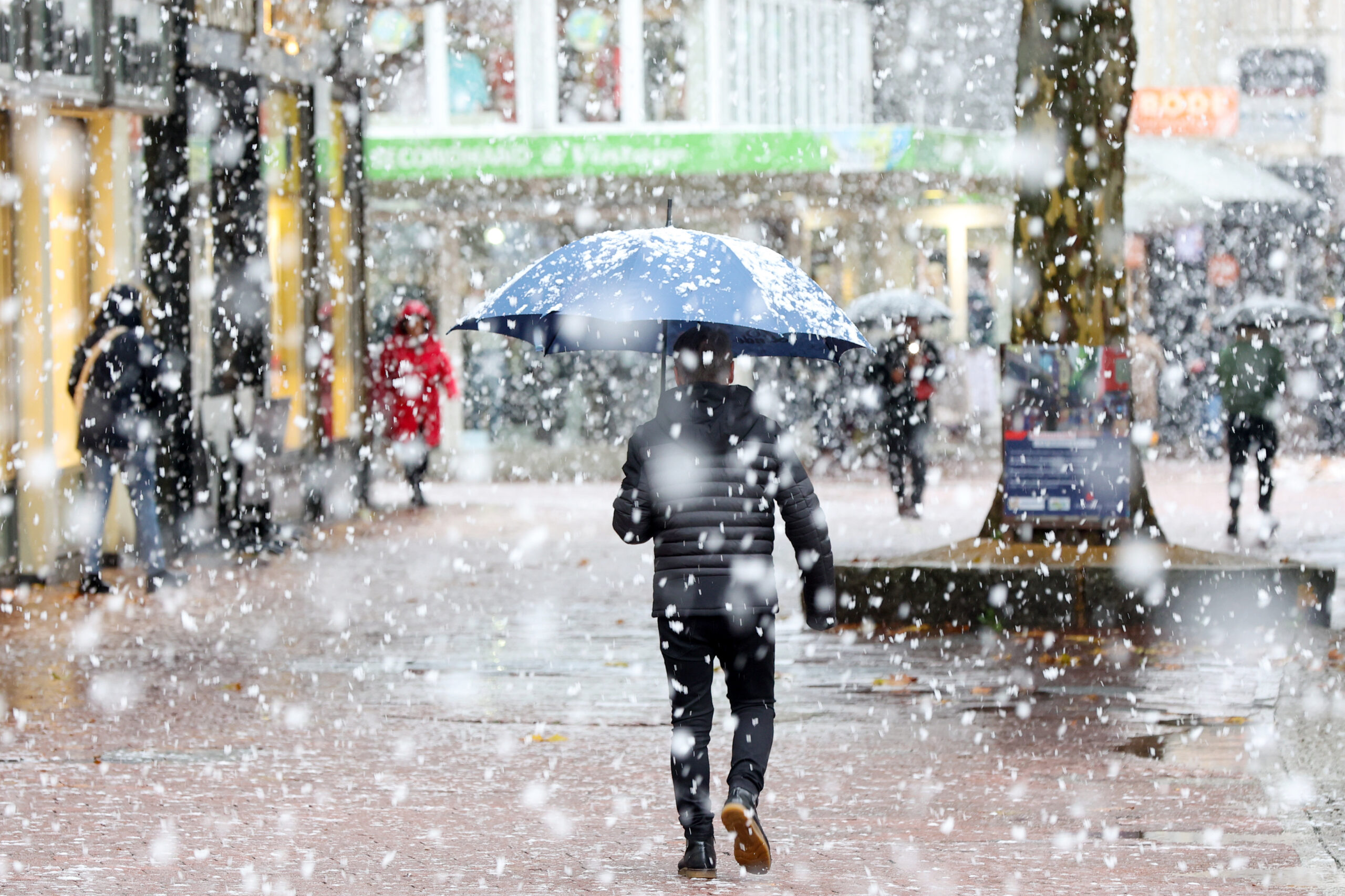 Ein Mann geht bei Schneefall durch die Fußgängerzone.