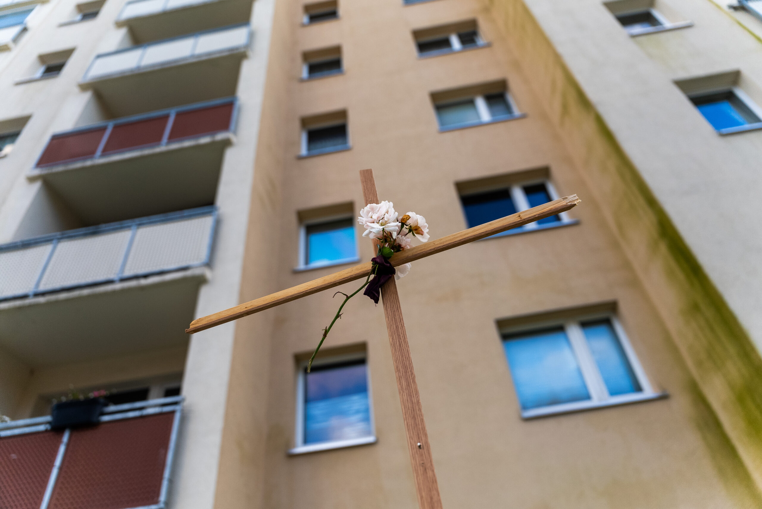 Ein Kreuz mit Blume steht vor einem Rostocker Hochhaus.