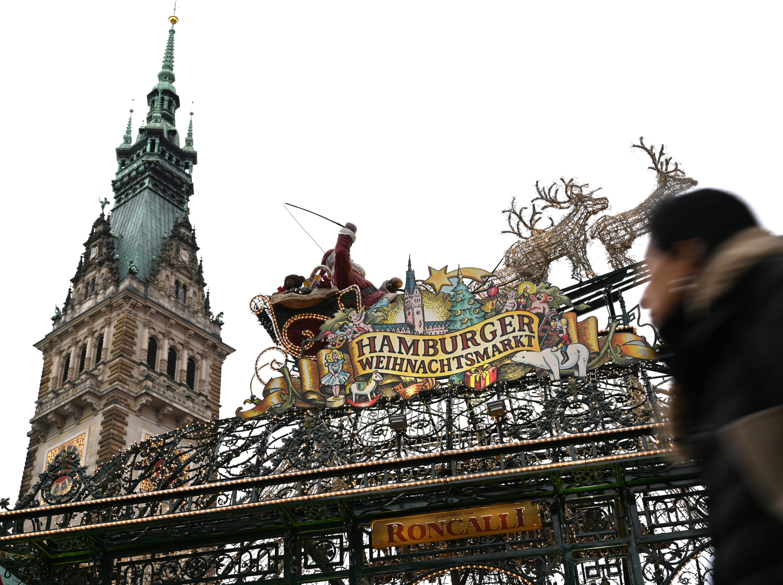 Eine Frau (r) geht am Eingang des Hamburger Weihnachtsmarktes vorbei, während im Hintergrund das Rathausgebäude zu sehen ist.