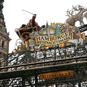 Eine Frau (r) geht am Eingang des Hamburger Weihnachtsmarktes vorbei, während im Hintergrund das Rathausgebäude zu sehen ist.