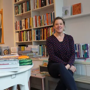 Tina, die Besitzerin des Koch Kontors sitzt auf einer Bank zwischen Bücherregalen im vorderen Teil ihres Ladens
