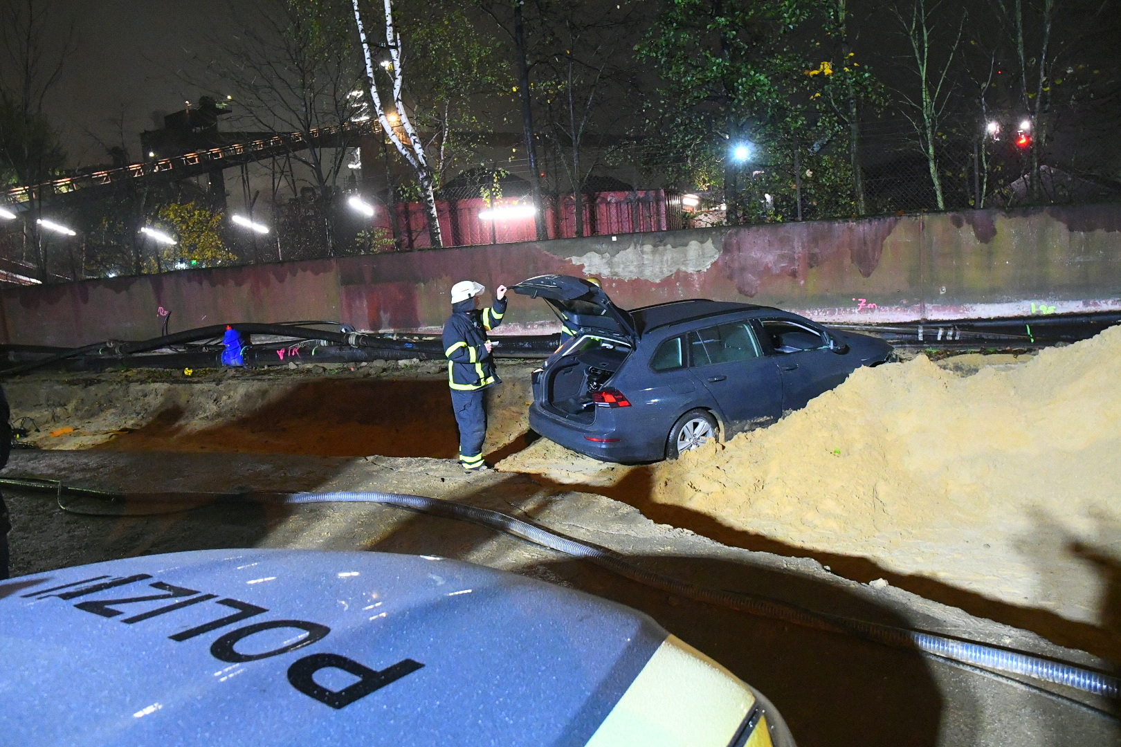 Auto steht in einem Sandhaufen. Polizist steht am Kofferraum