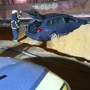 Auto steht in einem Sandhaufen. Polizist steht am Kofferraum