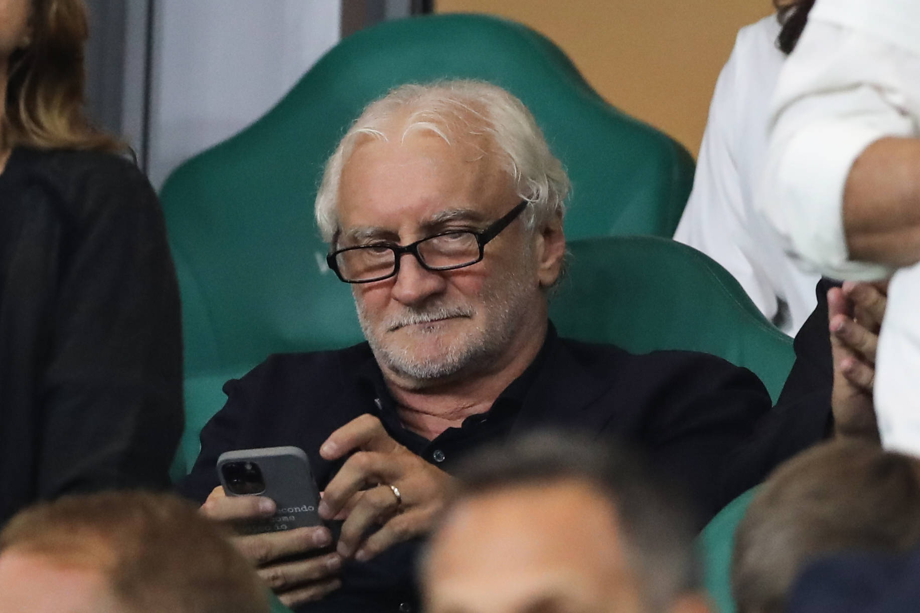 Rudi Völler scrollt mit Lesebrille auf dem Smartphone.