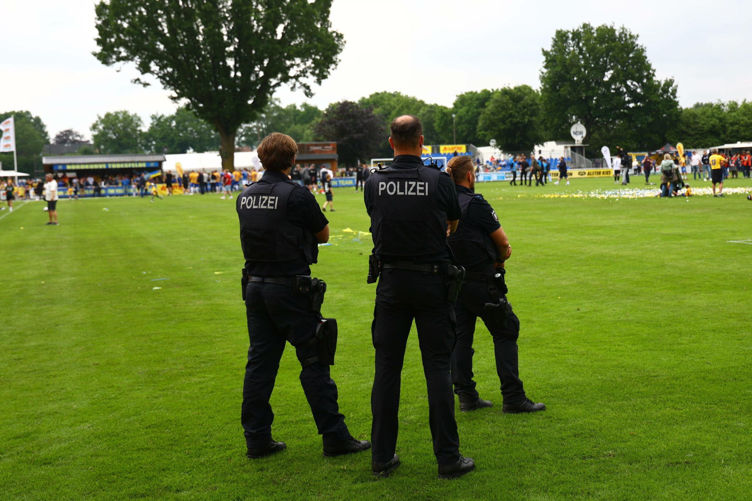 Drei Polizisten stehen am Rand eines Fußballfelds und beobachten die Lage