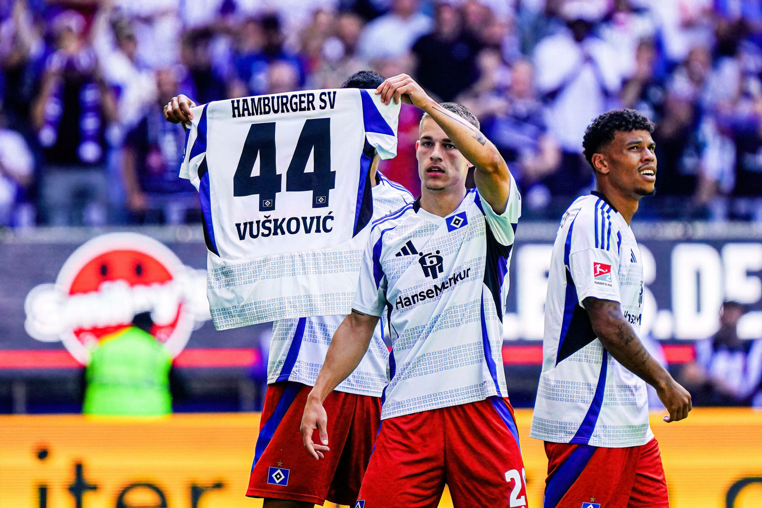 Miro Muheim hält ein Vuskovic-HSV-Trikot hoch.