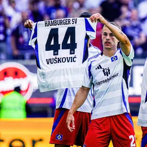 Miro Muheim hält ein Vuskovic-HSV-Trikot hoch.