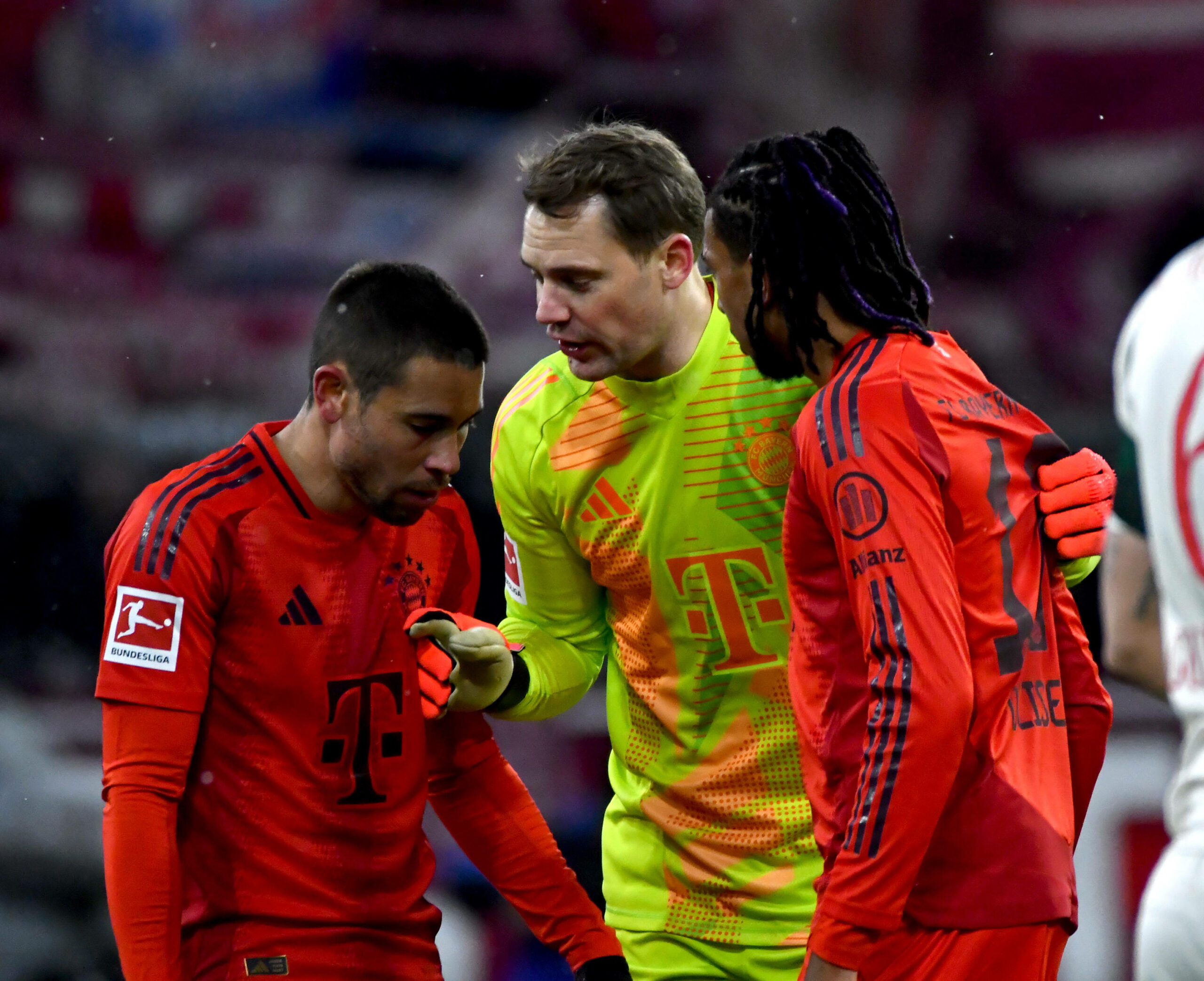 Michael Olise (r.) bekommt Anweisungen von Manuel Neuer (M.).