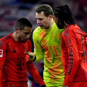 Michael Olise (r.) bekommt Anweisungen von Manuel Neuer (M.).