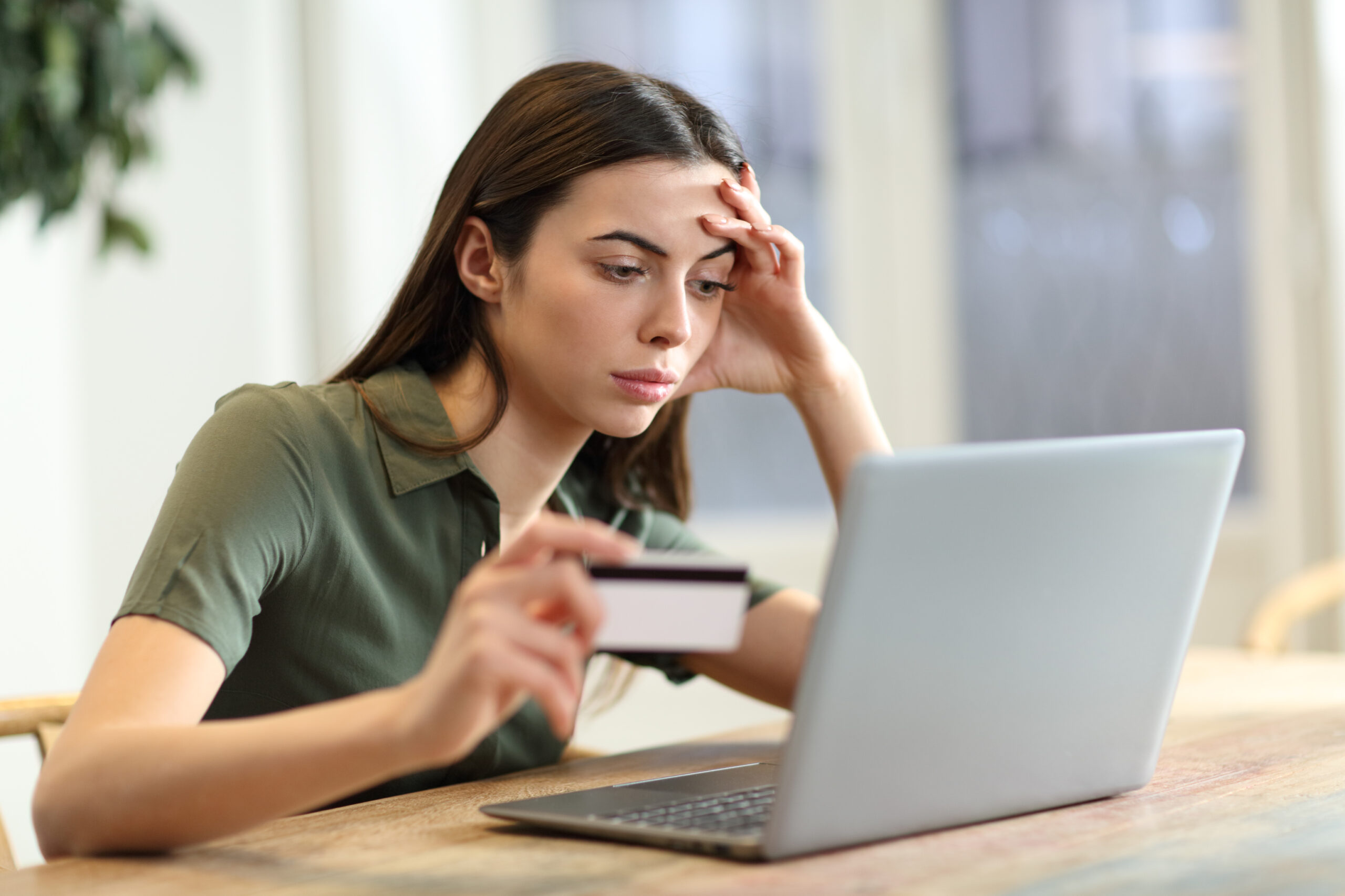 Eine Frau schaut besorgt auf ihren Laptop. In der Hand hält sie eine Bankkarte.