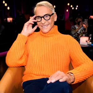 Ein älterer Mann sitzt in einem orangenen Pullover auf einem Ledersessel
