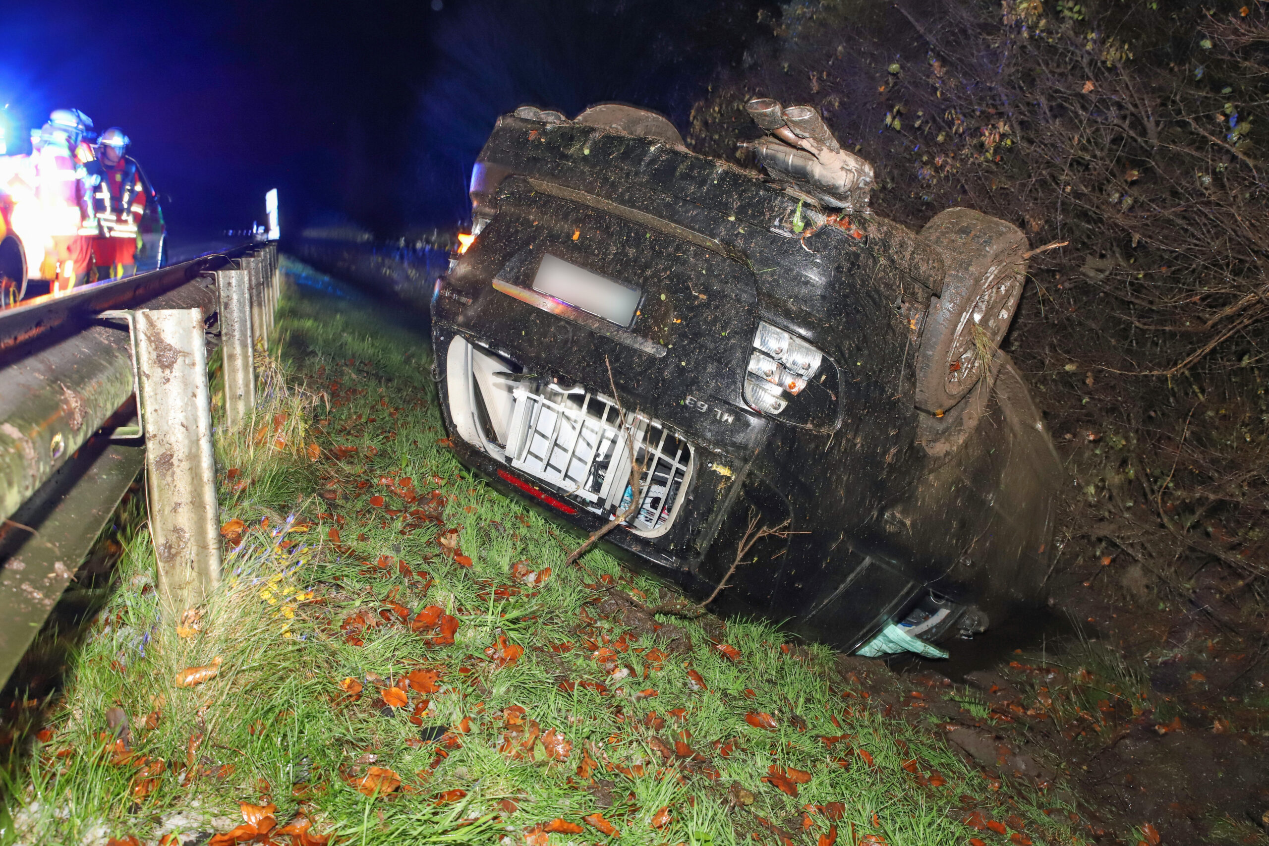 Ein dunkles Auto liegt beschädigt auf dem Dach hinter einer Leitplanke