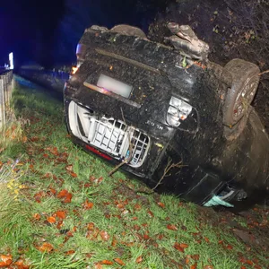 Ein dunkles Auto liegt beschädigt auf dem Dach hinter einer Leitplanke