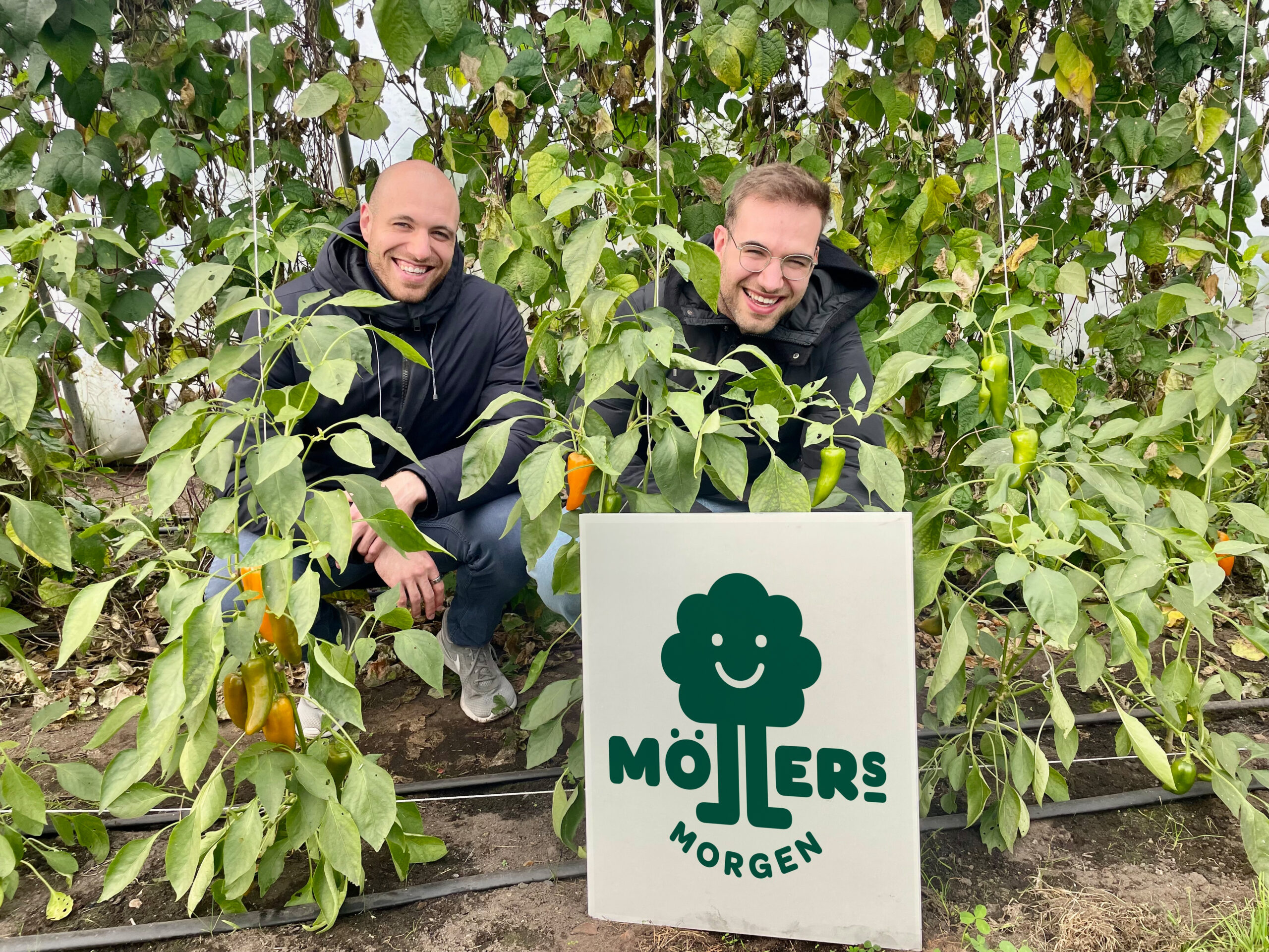 Zwei junge Männer inmitten von Bäumen und mit einem Schild: „Möllers Morgen“