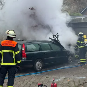 AUs einem Auto steigt Rauch auf. Die Feuerwehr löscht