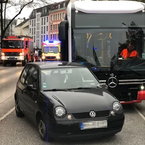 Ein PKW steht mit leicht beschädigtem Außenspiegel vor einem Bus. Im Hintergrund stehen Feuerwehr und Rettungskräfte