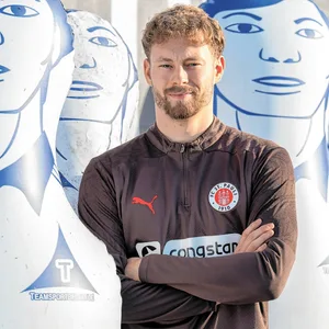 Carlo Boukhalfa grinst mit verschränkten Armen in die Kamera