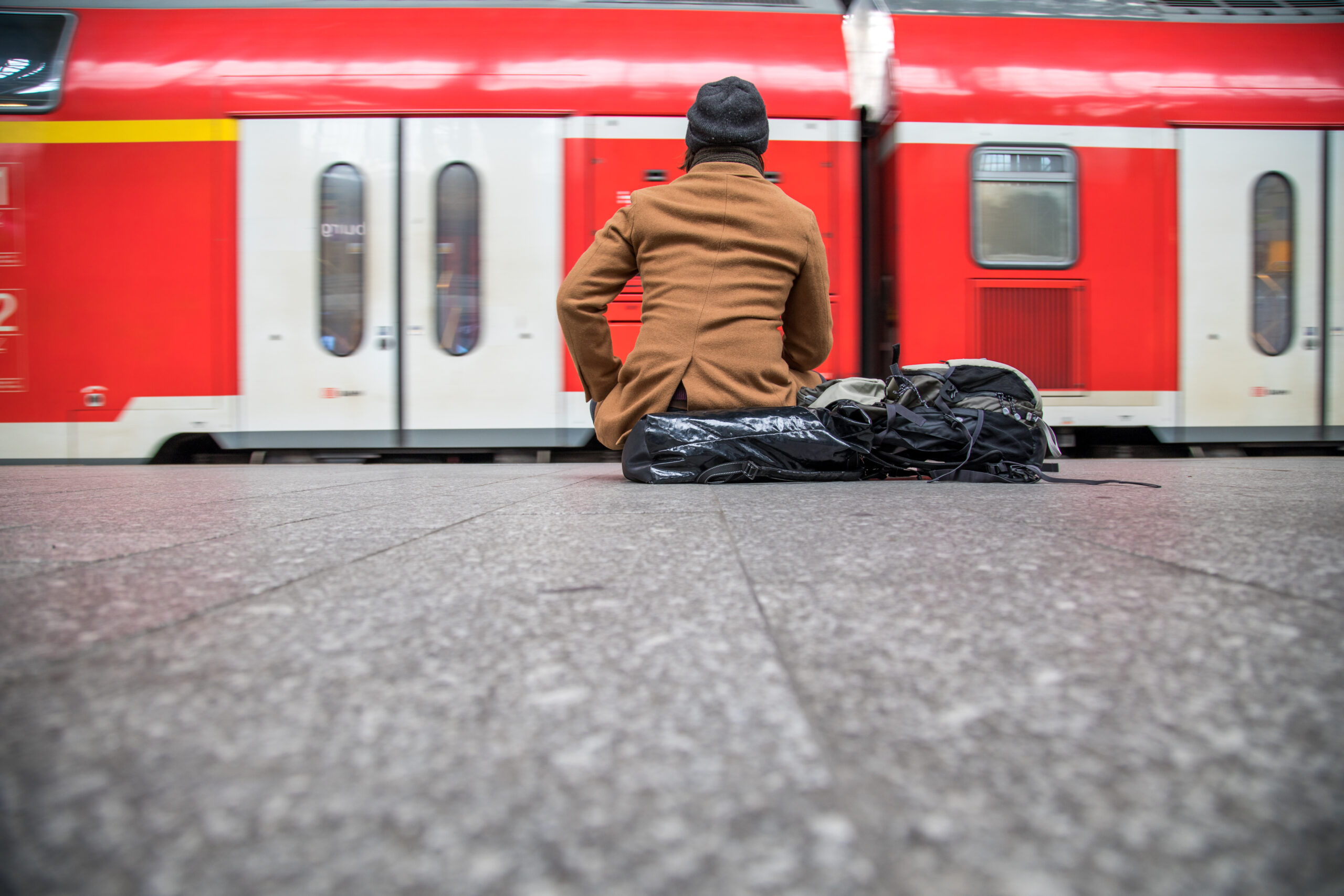 Ein Mann sitzt mit seiner Tasche am Gleis