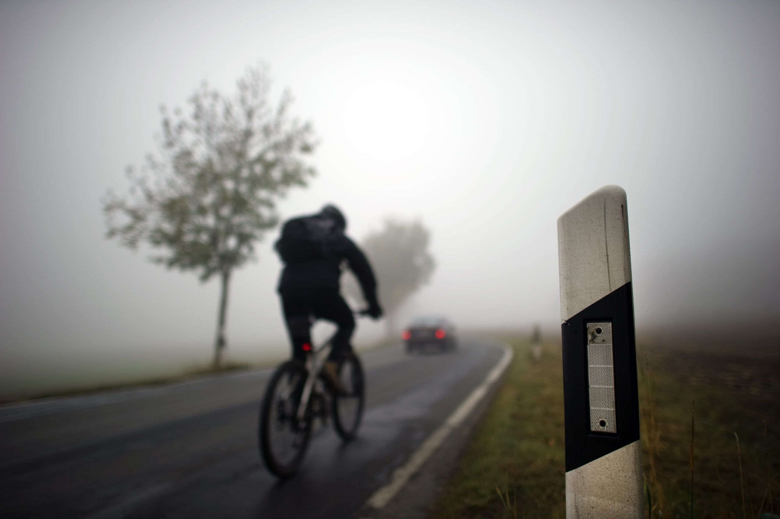 Ein Radfahrer fährt durch dichten Nebel auf einer Landstraße.