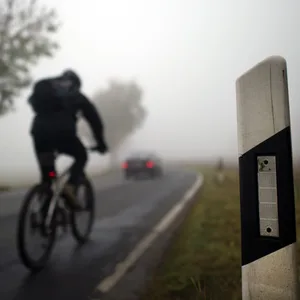 Ein Radfahrer fährt durch dichten Nebel auf einer Landstraße.