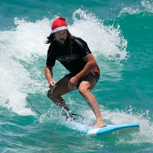 Ein Mann mit Weihnachtsmütze steht auf einem Surfbrett