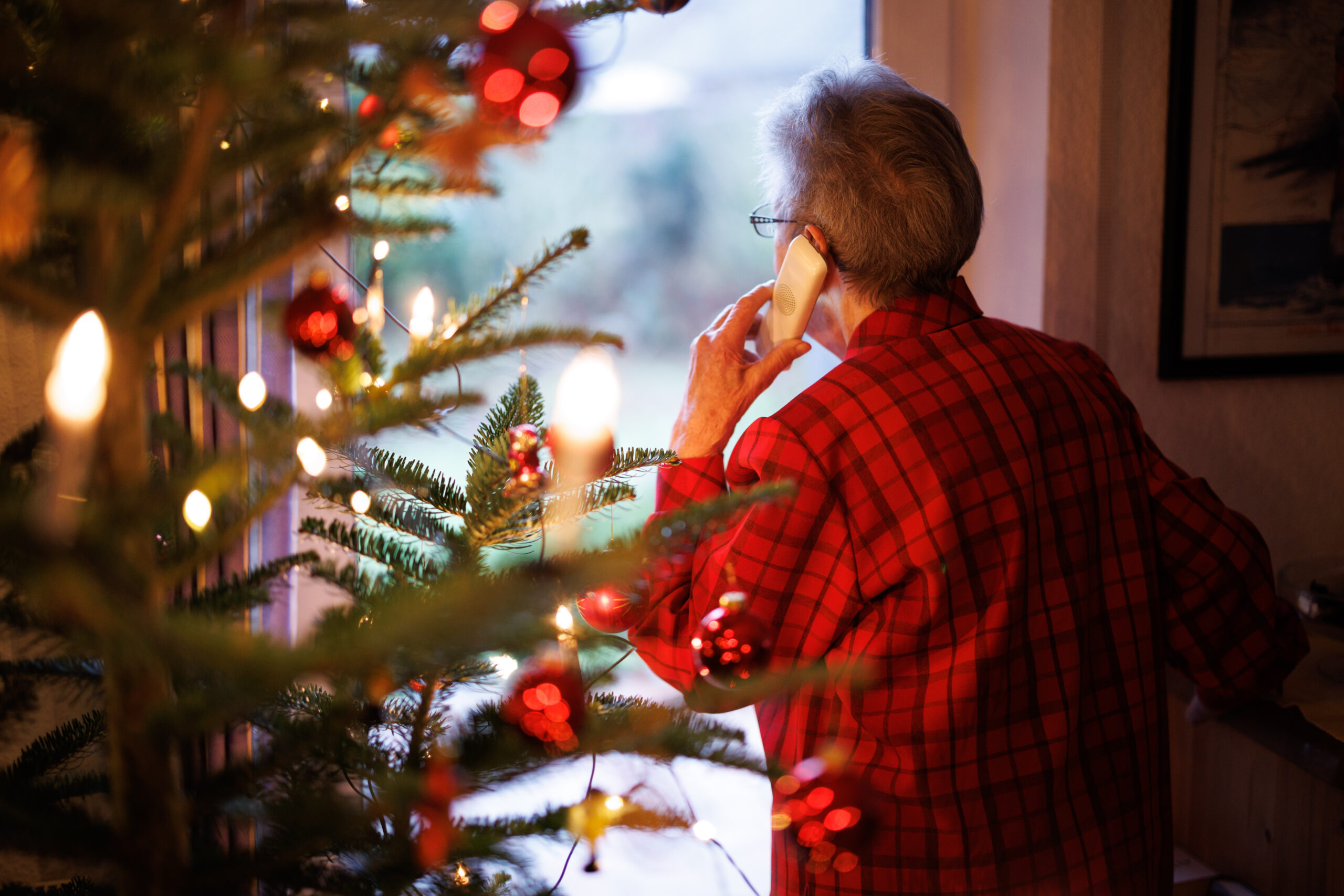 Eine Frau steht neben ihrem Tannenbaum am Fenster und telefoniert