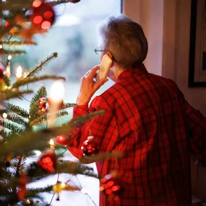 Eine Frau steht neben ihrem Tannenbaum am Fenster und telefoniert