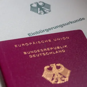 Eine Einbürgerungsurkunde der Bundesrepublik Deutschland und ein deutscher Reisepass liegen auf einem Tisch.