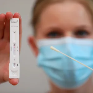 Positives Testergebnis eines Corona-Schnelltests. Eine Dame mit OP-Maske zeigt das positive Ergebnis in die Kamera.