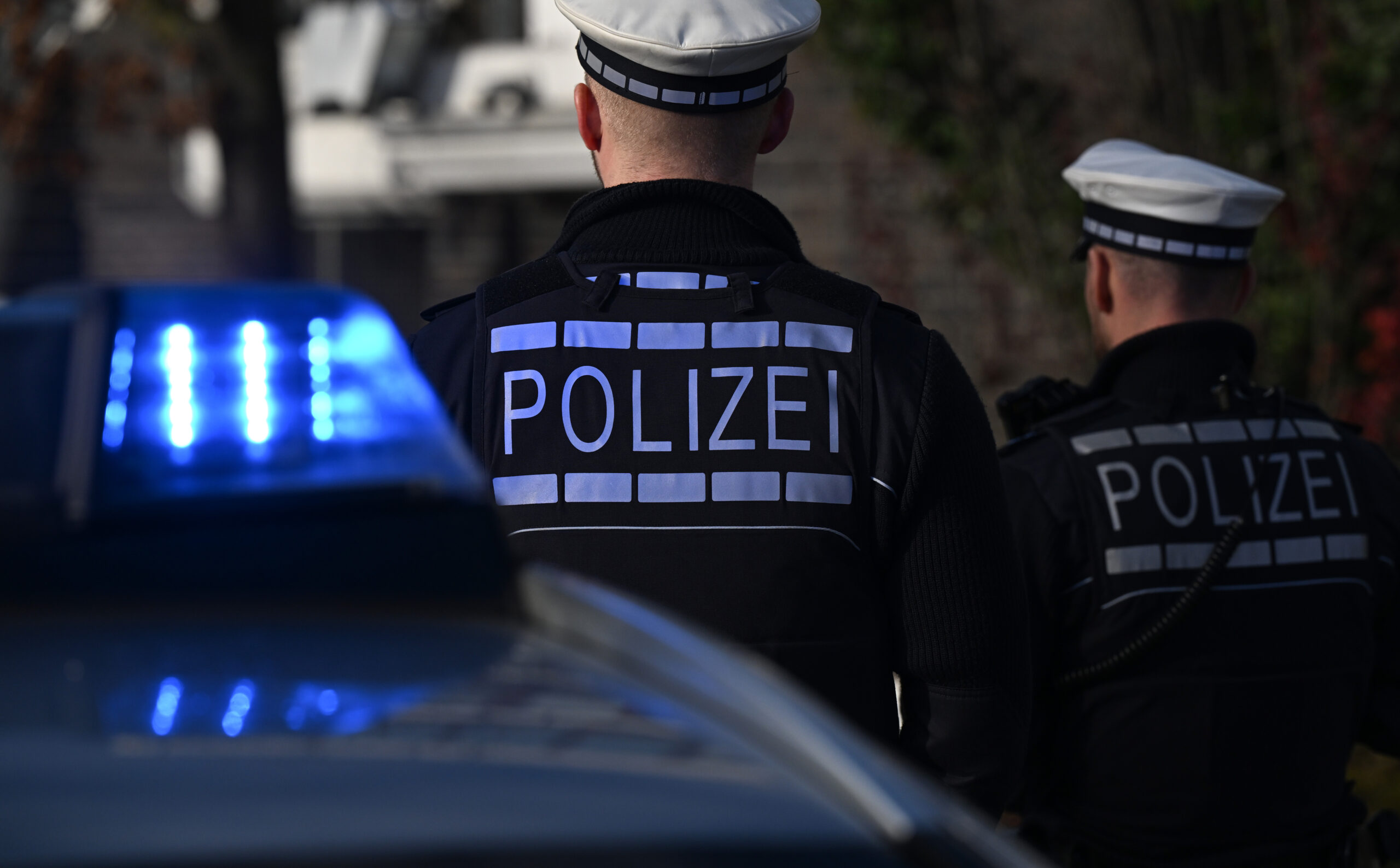 Das Logo der Polizei auf der Dienstkleidung von Polizisten die vor einem Blaulicht stehen.