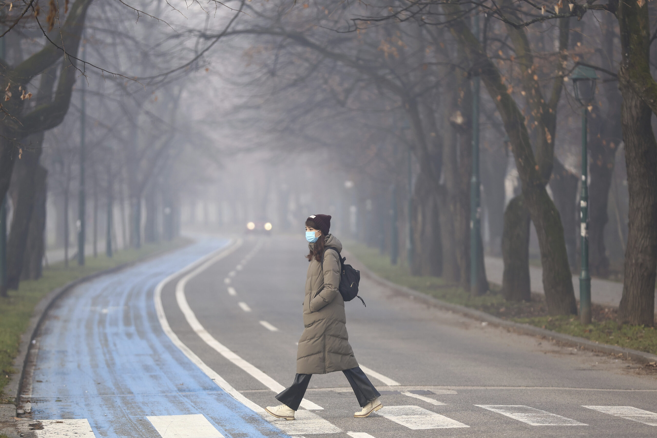 Eine Frau trägt einen Mund-Nasen-Schutz und überquert eine Straße, während der Smog Sarajevo bedeckt