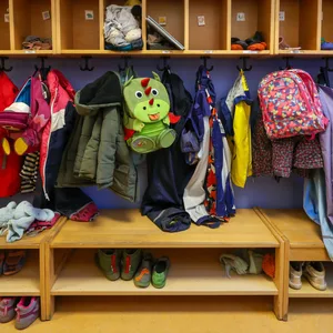 Maentel, Jacken, und Rucksäcke von Kindern hängen an einer Garderobe in einem Kindergarten.