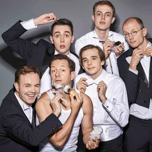 Die sechs Schauspieler stehen in einem Frack gekleidet zusammen.