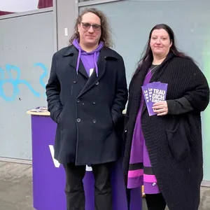Mann udn Frau vor einem lila Info-Stand