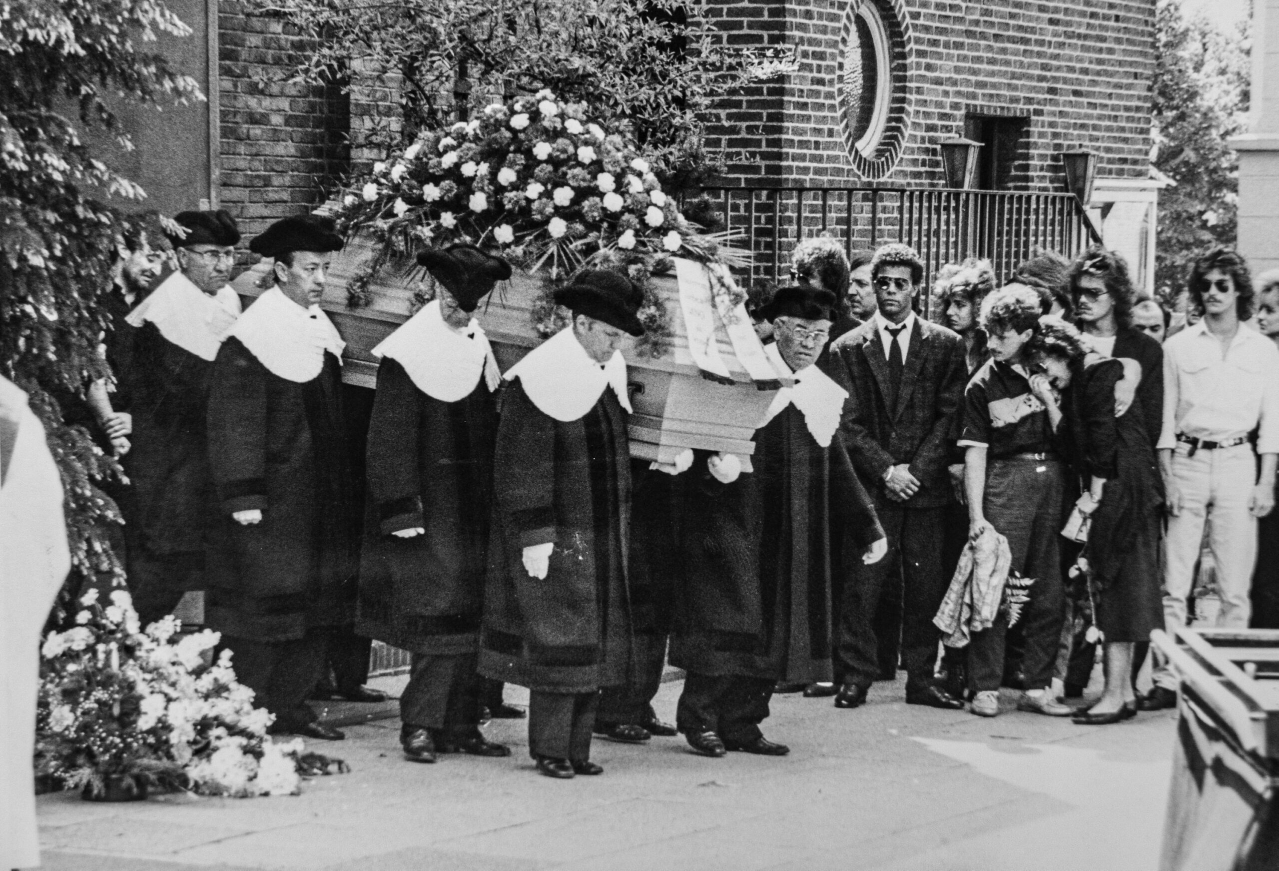 Sargträger tragen einen Sarg mit Blumen aus einer Kapelle