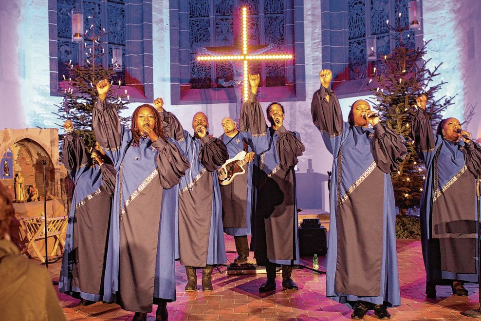 Männer und Frauen des Chores stehen in einer Kirche und singen.