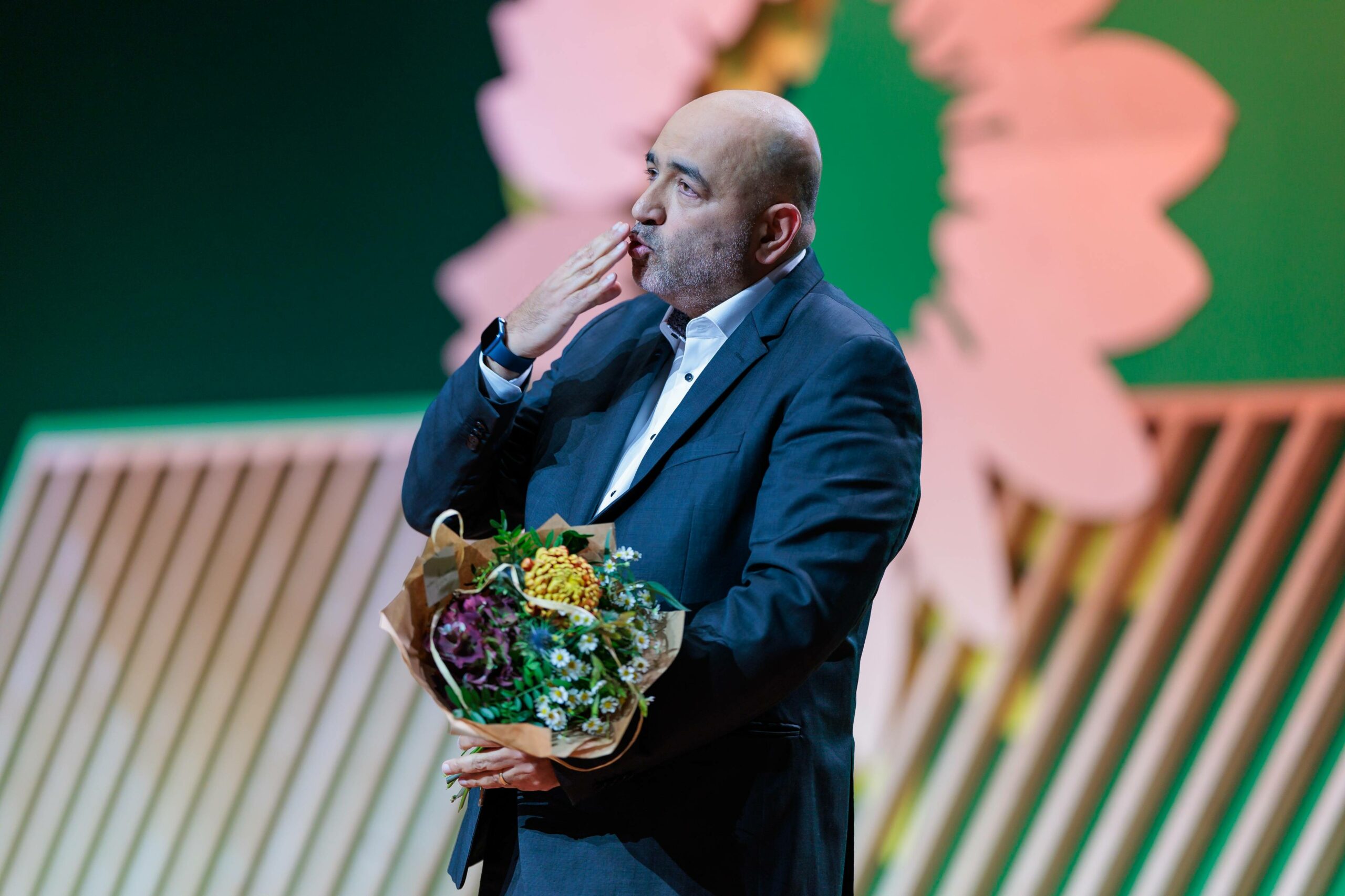 Omid Nouripour gibt nach seiner Abschiedsrede beim Grünen-Bundesparteitag einen Handkuss mit Blumenstrauß in der Hand.