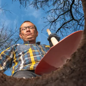 EIn Mann mit Schaufel steht vor einem gegrabenen Loch.