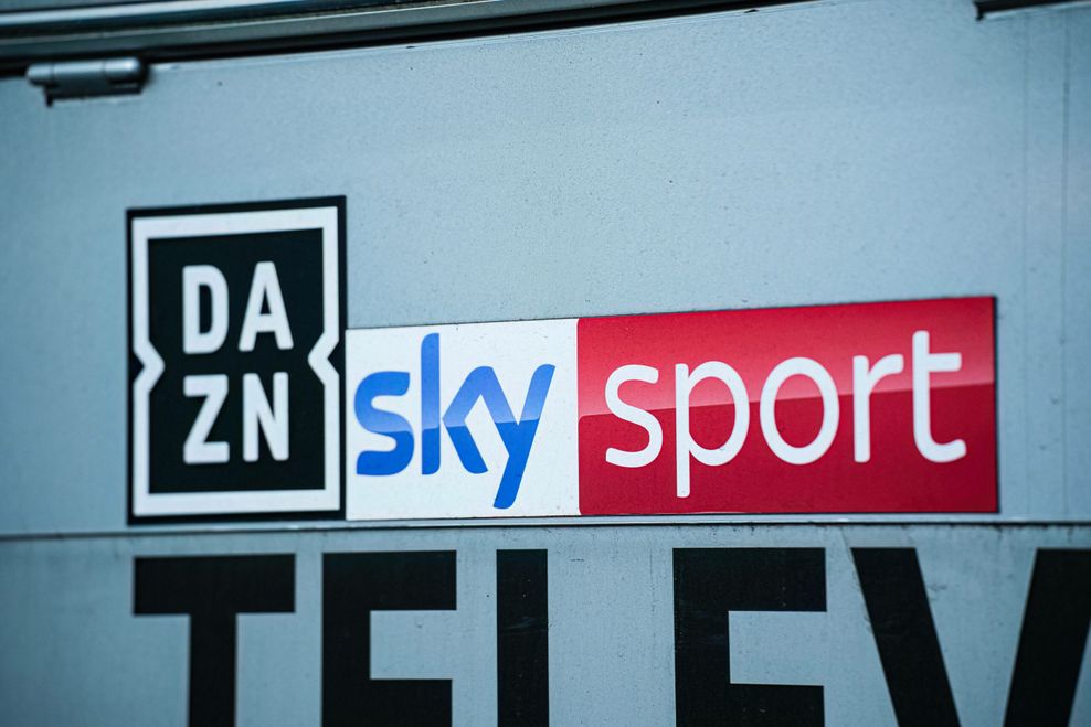 DAZN-Logo und Sky-Logo auf einer grauen Wand.