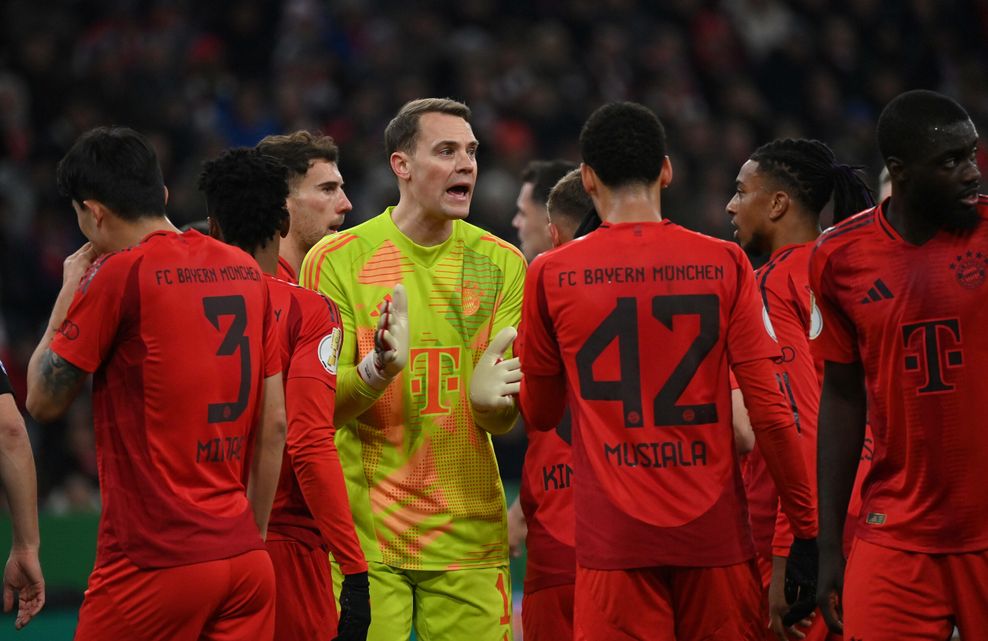 Manuel Neuer klatscht in die Hände während viele Mitspieler um ihn herumstehen.