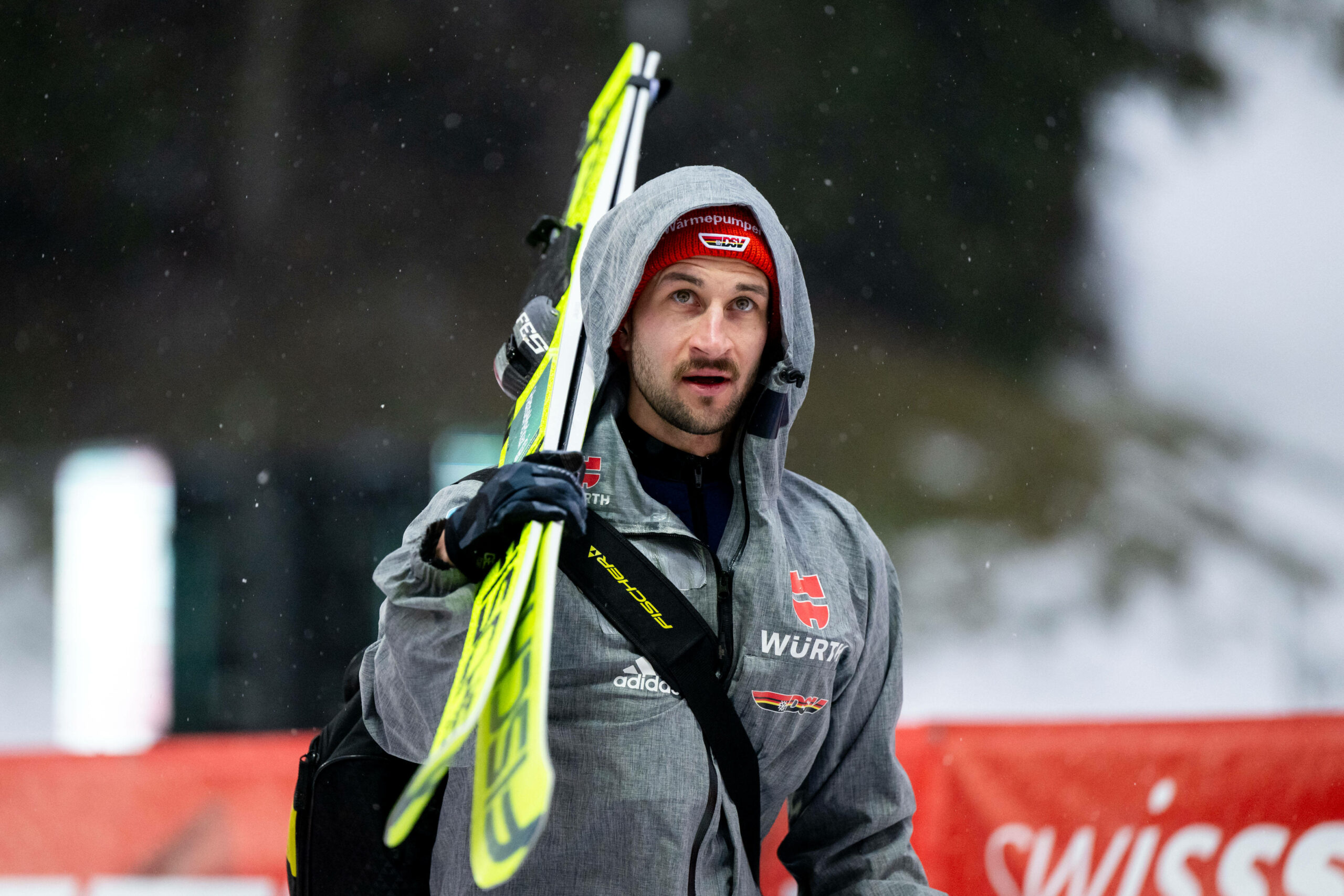 Markus Eisenbichler schaut nach oben und trägt seine Ski.