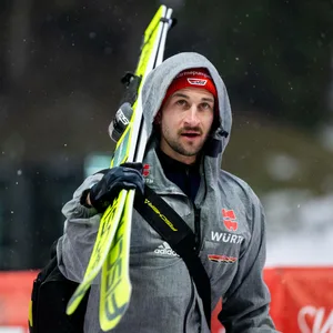 Markus Eisenbichler schaut nach oben und trägt seine Ski.