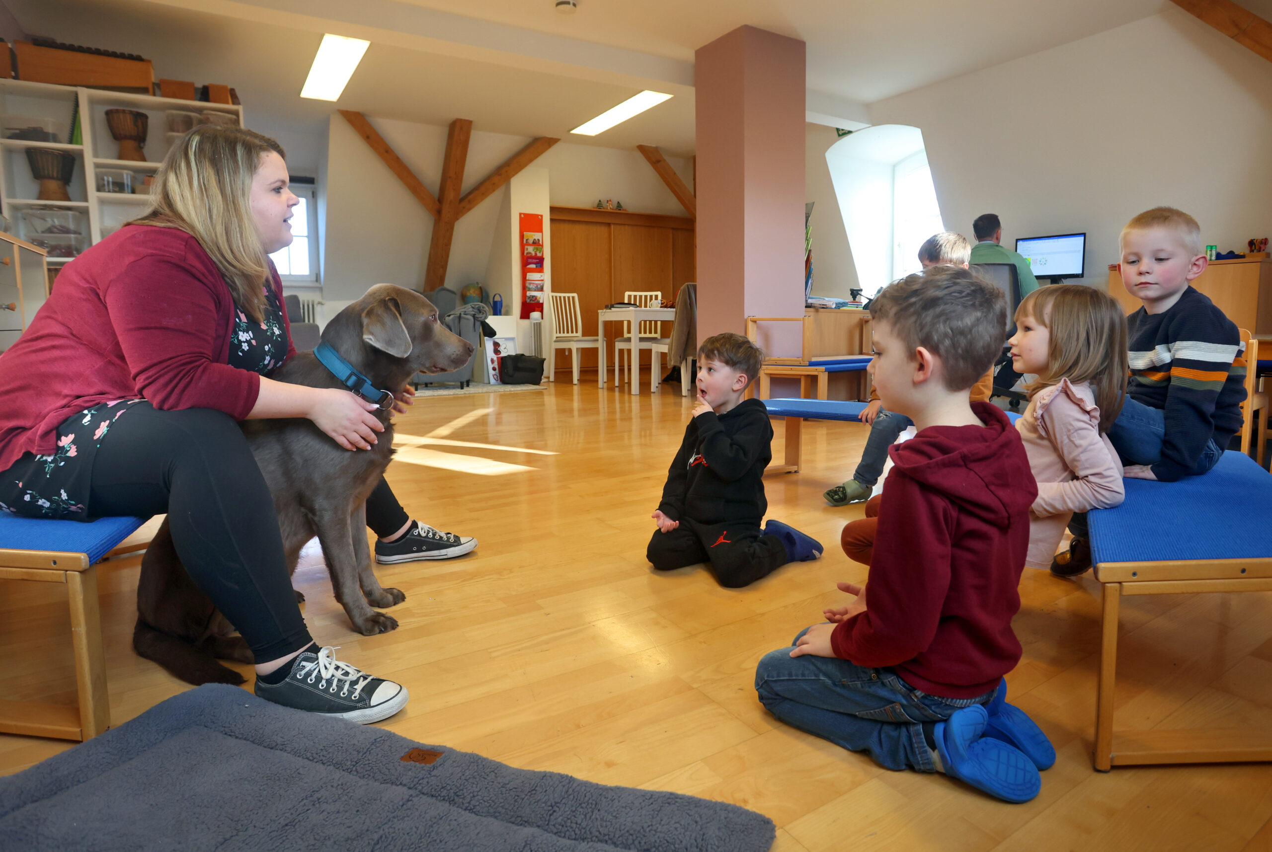 Erzieherin sitzt mit Kindergartenkindern in einem Kreis