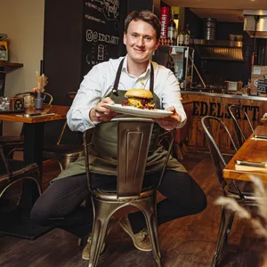 „Edelsatt“-Mitarbeiter Max Schippmann serviert einen Burger mit Wildfleisch.