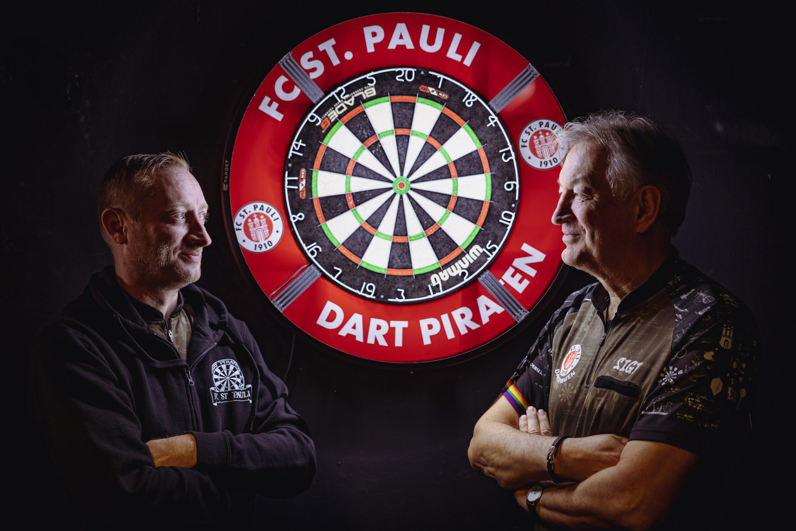 Gunnar Wendorf und Sigi Faßbinder stehen vor einer Dartsscheibe und schauen sich an