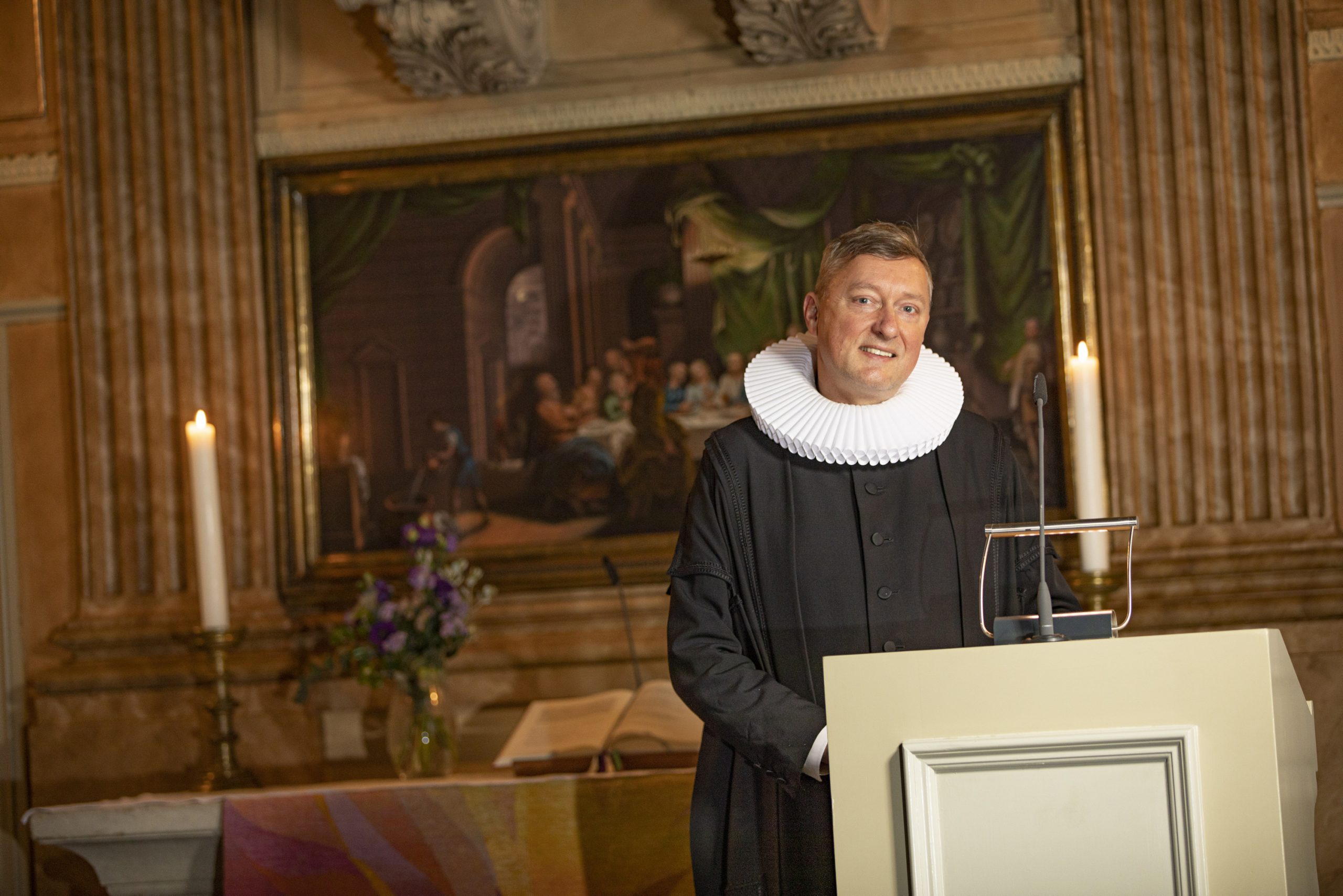 Pastor mit weißer Halskrause vor Altar