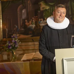 Pastor mit weißer Halskrause vor Altar
