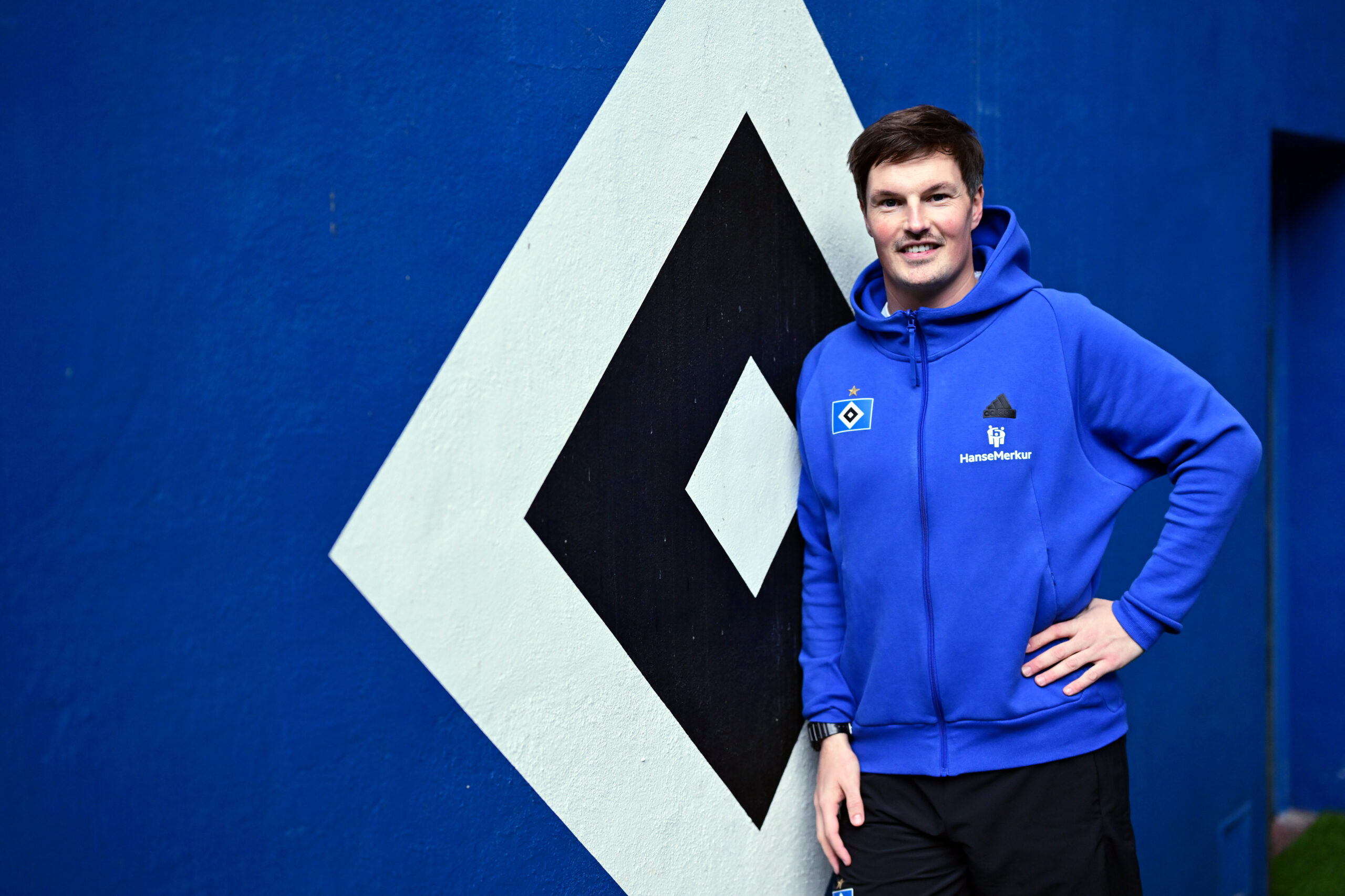 Trainer Merlin Polzin steht vor dem HSV-Logo.