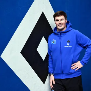 Trainer Merlin Polzin steht vor dem HSV-Logo.